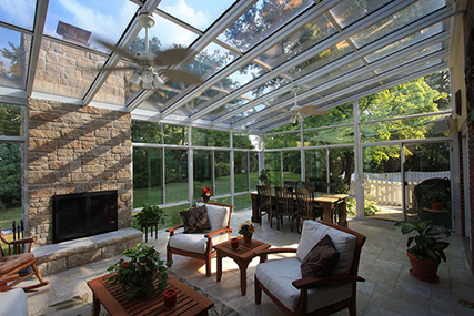 Image Alt TeInterior of a sunroom with a dining room table, outdoor chairs and a coffee table, and a fireplace with a ceiling fan overhead. xt